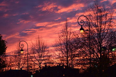 Silhouette of bare trees against cloudy sky at sunset