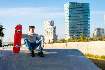 Young boy sitting on skatepark ramp holding a skateboard, looking away