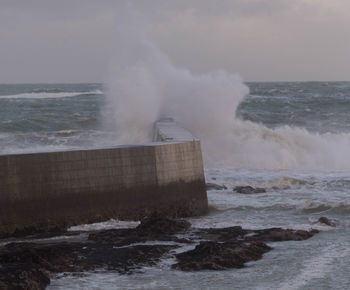 Waves splashing on retaining wall against sky