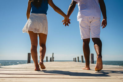 Rear view of couple walking on jetty during sunny day