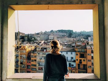 Rear view of young woman standing by cityscape against sky