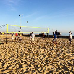 People playing beach volleyball against sky during sunny day