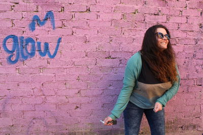 Portrait of young woman standing against wall