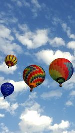 Low angle view of hot air balloons flying against cloudy sky