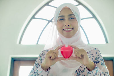 Portrait of a smiling young woman holding heart