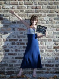 Portrait of smiling girl with message standing against brick wall