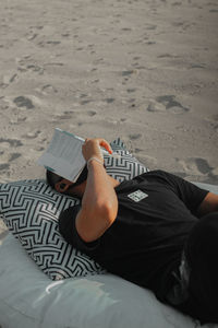 Young man holding book lying on beach