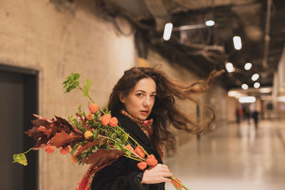 Portrait of woman holding bouquet while standing in corridor