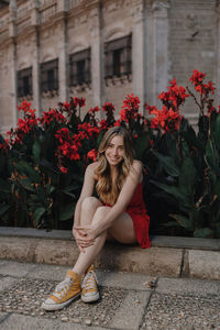 Portrait of smiling young woman with red flowers in front of building