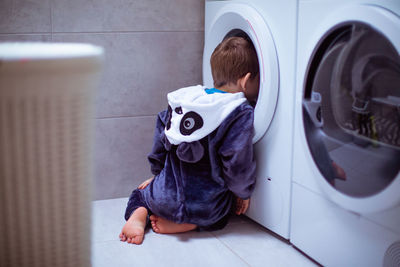 Rear view of boy peeking in washing machine