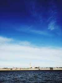 View of factory by sea against blue sky