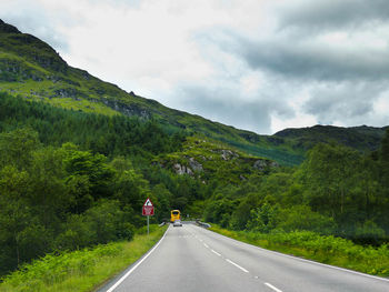 Road amidst trees on mountain against sky