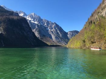 Scenic view of lake by mountains against clear blue sky