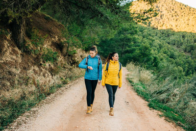 Rear view of friends standing on dirt road in forest