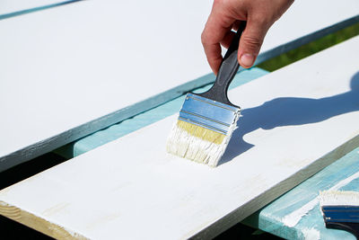 Male builder paints white boards for construction. male hand holds brush. painting work