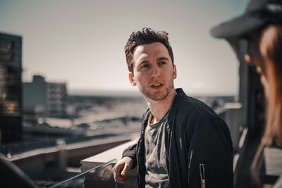 Portrait of young man against city in sky