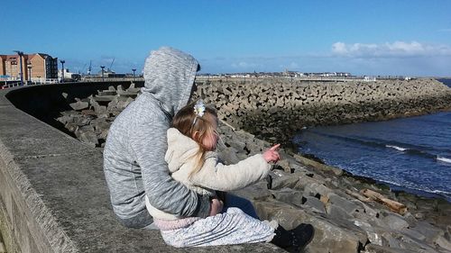 Father with daughter sitting on retaining wall by groyne at seashore