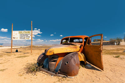 Abandoned car on landscape against clear blue sky