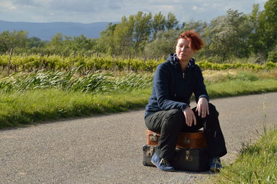 Full length of woman sitting on suitcases over road