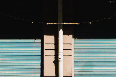 String hanging by pipe amidst closed shutters on sunny day