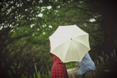 Midsection of people behind umbrella amidst trees on road