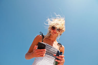 Low angle view of woman using mobile phone against clear blue sky