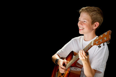 Young man playing guitar against black background