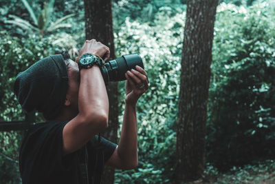 Full length of man photographing against trees in forest