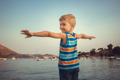 Portrait of cute smiling boy standing at beach against clear sky