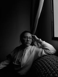 Portrait of young woman sitting on chair at home looking though the window 