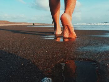 Low section of man standing on beach against sky