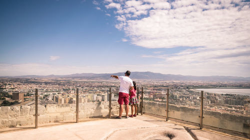 Rear view of man standing on railing against sky