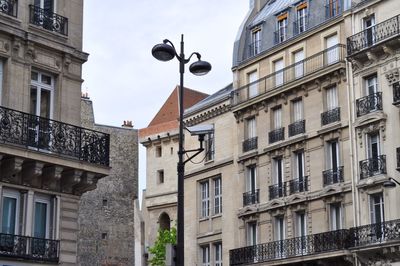 Low angle view of security camera on street light amidst buildings against sky