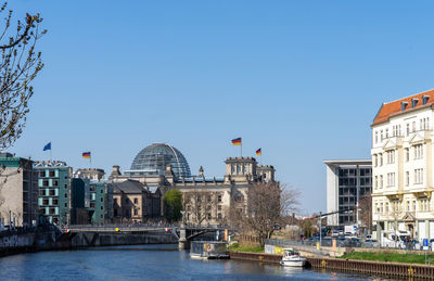 View of buildings by river against clear sky