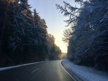 Road amidst trees seen from car windshield against sky during winter