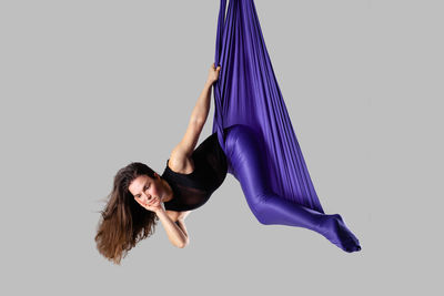 Woman with purple textile dancing against gray background