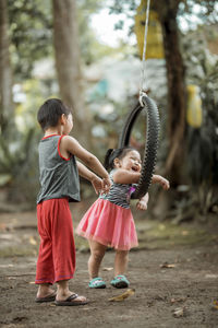 Siblings playing with tire swing in playground