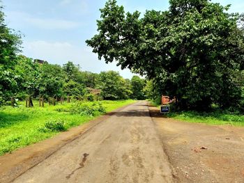 Dirt road amidst trees against sky