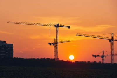 Silhouette cranes at construction site against sky during sunset