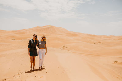 Portrait of smiling young woman with friend walking at desert against sky