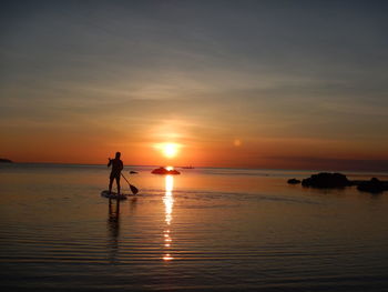 Man in sea against sunset sky