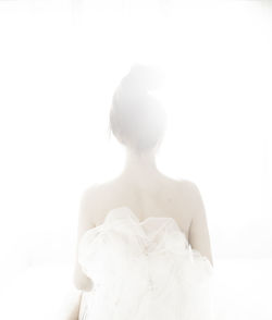 Rear view of bride in wedding dress sitting against white background