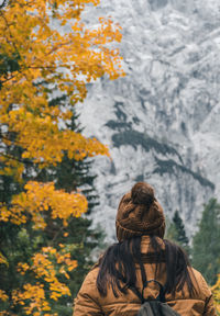 Rear view of woman wearing warm clothes and knit hat, walking toward mountains in autumn