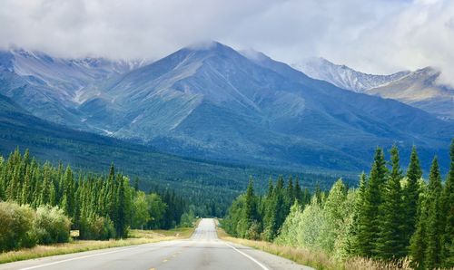 Road amidst trees and mountains against sky