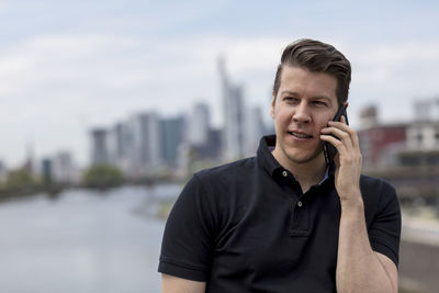 Young man talking on mobile phone with city in background