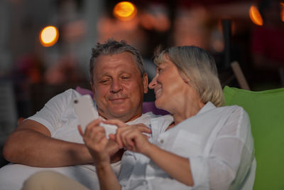 Smiling mature woman showing mobile phone to man at night