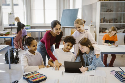 Teacher with male and female students using tablet pc at desk in classroom