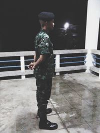Side view of young man standing against bench at night