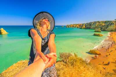 Woman holding cropped hand against sea