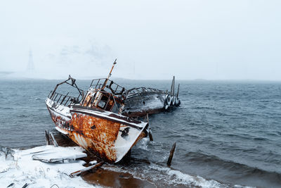 Abandoned boat in sea against sky during winter